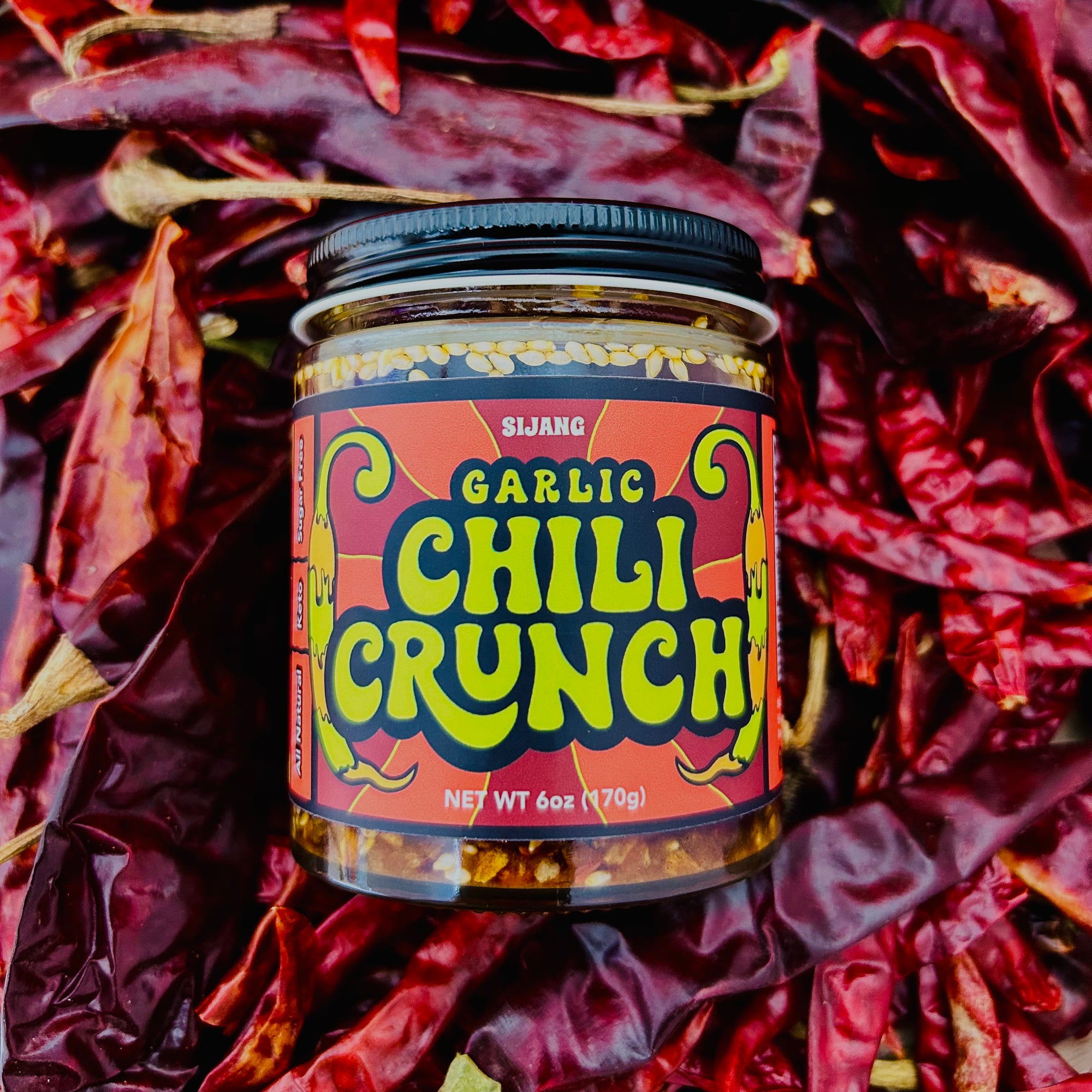 jar of SIJANG chili crunch on laying on top of a bunch of peppers
